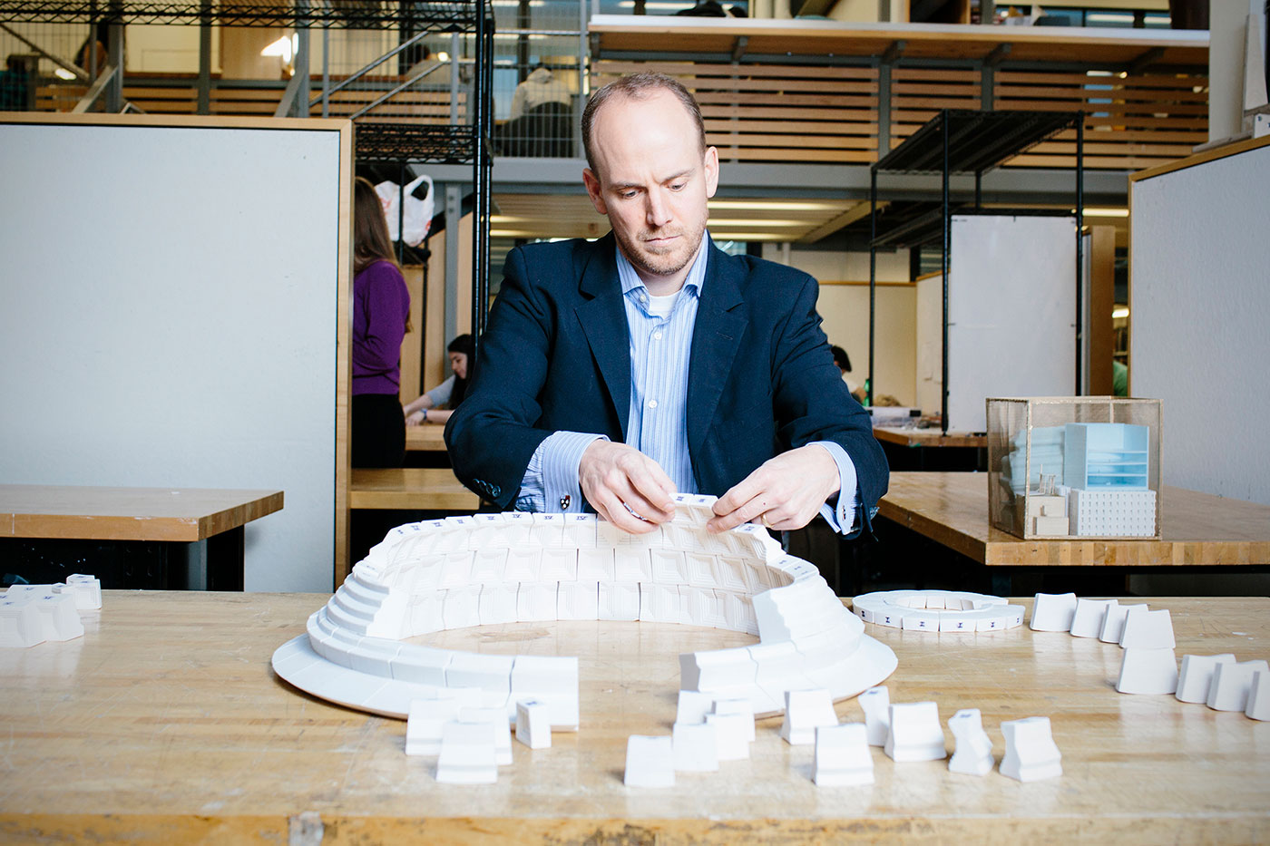 Man assembles a large architectural model on a table inside a classroom