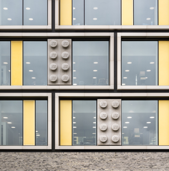A glass facade with yellow stripes and concrete Lego bricks