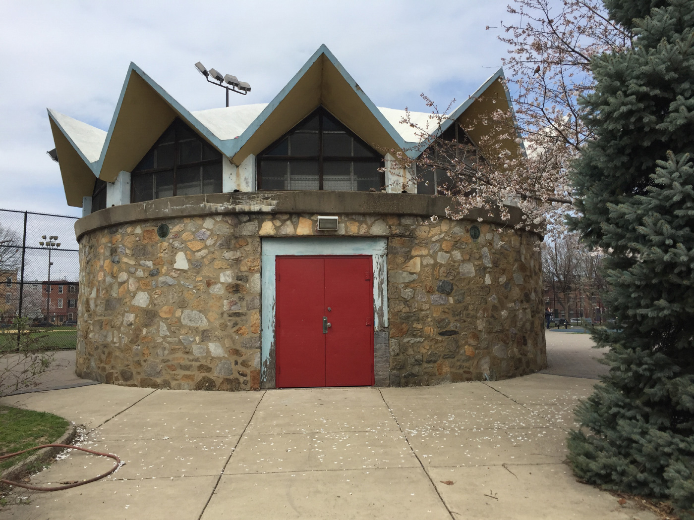 Photo of the Columbus Square pavilion, a small, circular structure with thick stone walls, a single red door, and an angular roof.