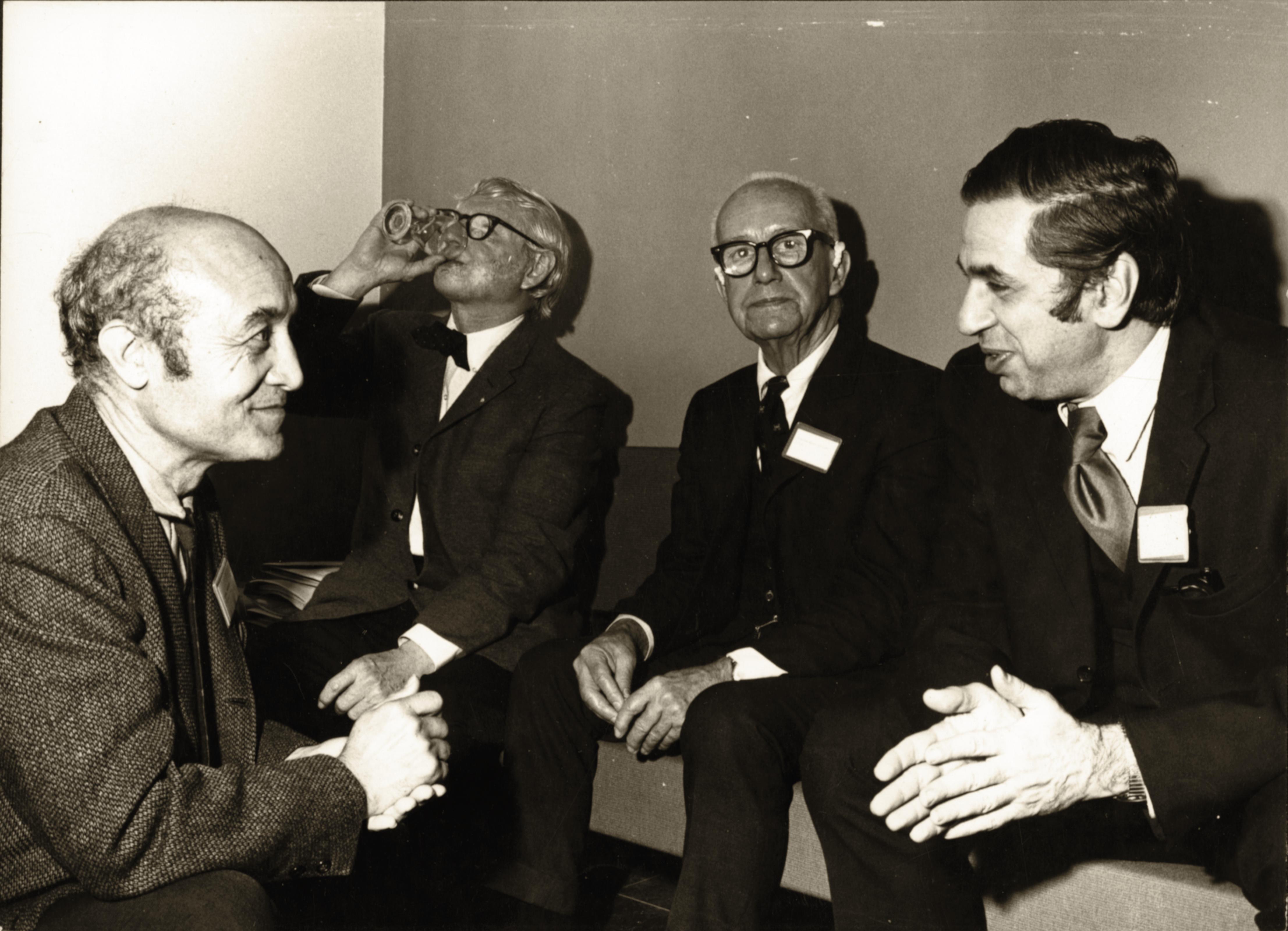 A black and white photo of four men talking and drinking, including Isamu Noguchi