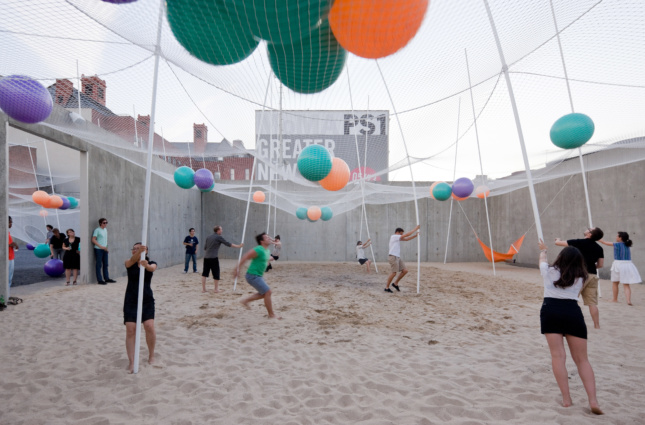 People playing in the sand beneath a net full of beach balls