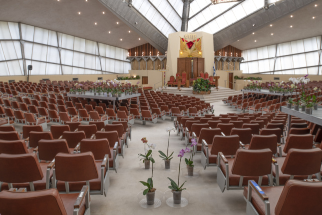 A large sanctuary with many seats and orchids on the floor and on platforms.