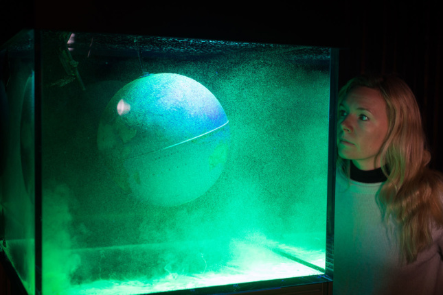 A woman looking into a tank with a globe covered in green mists