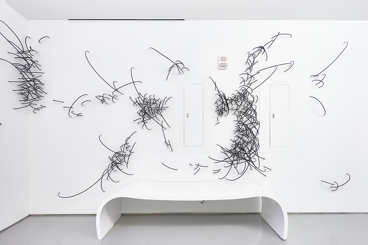 Sculpture of white bench in front of white wall with cable-like projections coming out