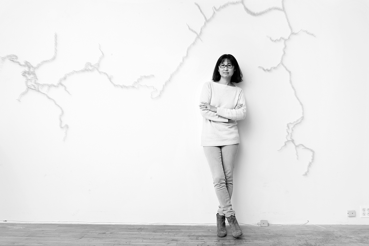 Black and white portrait of Maya Lin against a dead tree