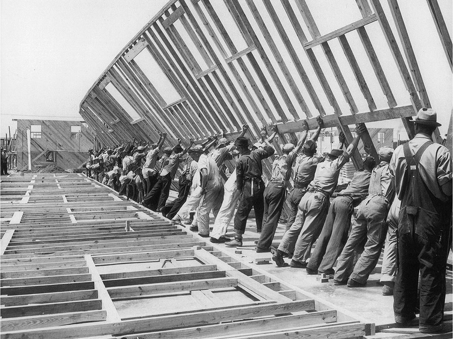 Black and white image of men lifting wood frame wall for house, part of the Venice Architecture Biennale