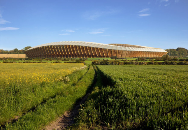 A timber-constructed football stadium sits in a field with blue skies