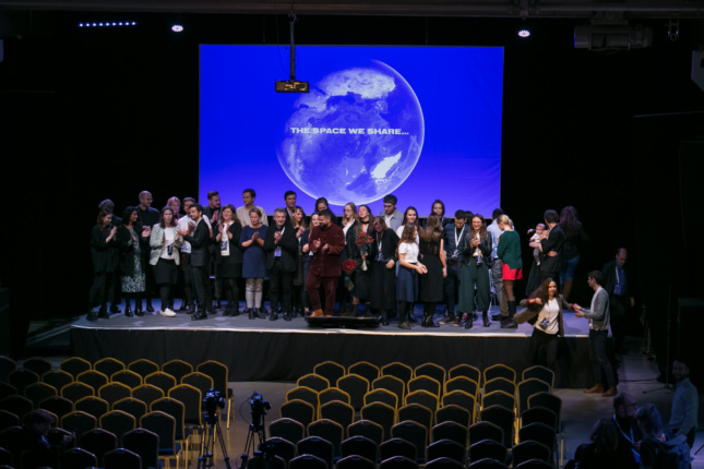 A group of people on stage at the Architecture of Migration conference