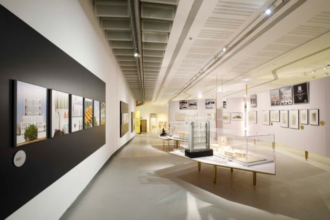 A gallery in a museum is filled with architectural models, photographs, and drawings