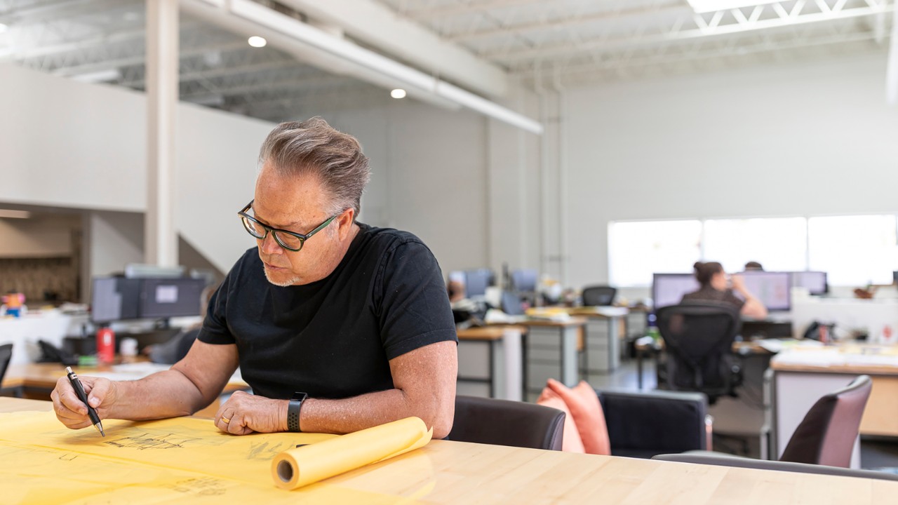 An architect sits at a work table with a roll of trace