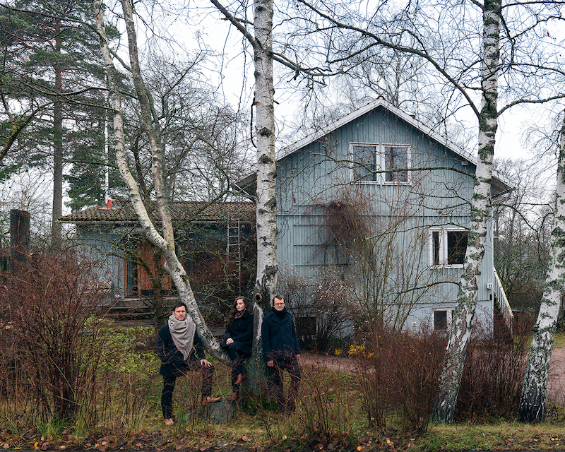 Image of three architecture curators in front of timber-clad house in the woods