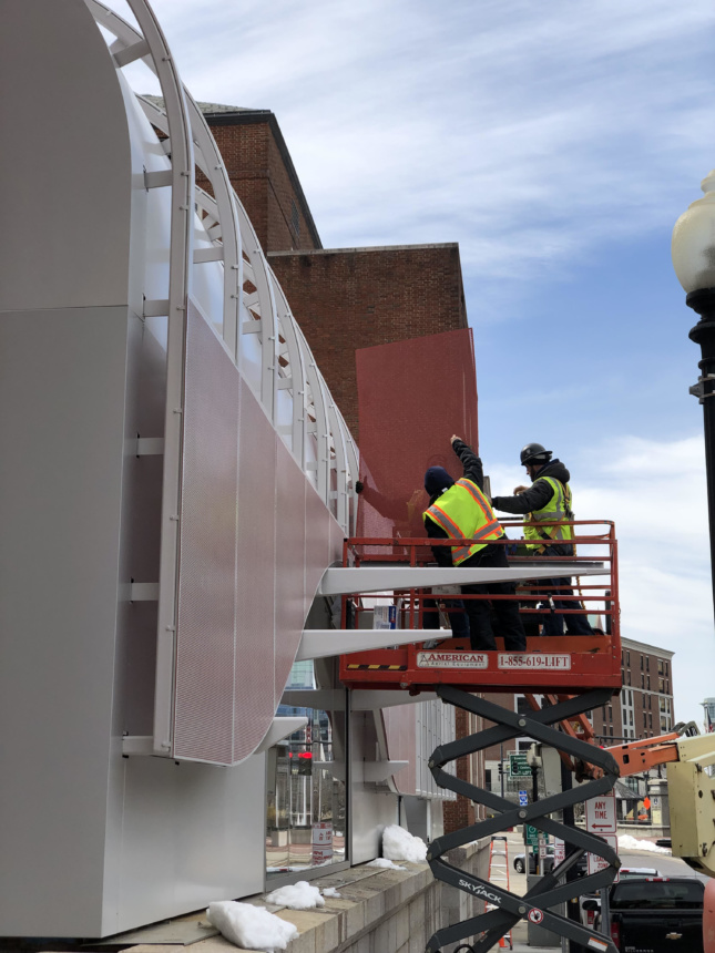 Construction workers installing a perforated aluminum facade