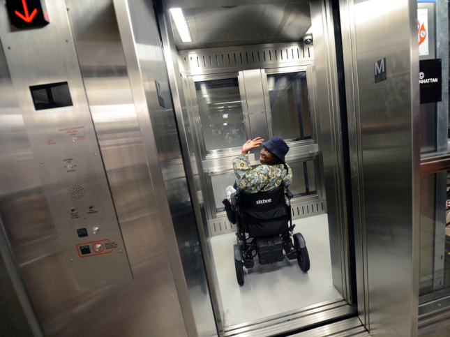 Image of woman in wheelchair waving inside subway station elevator