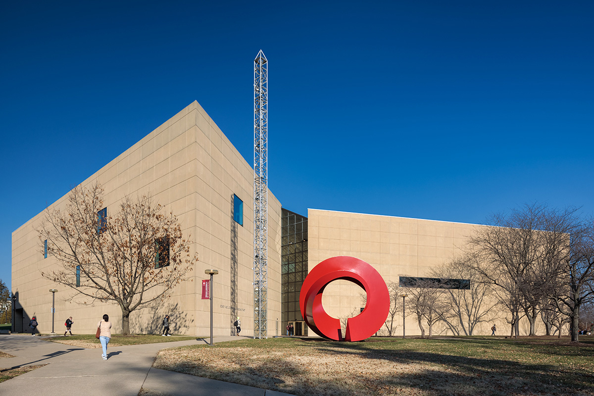 Exterior image of a limestone-clad museum and red circular sculpture in its front lawn