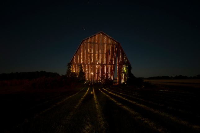 A barn at night with light coming out through the holes
