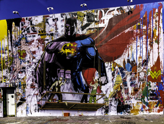 A Mr. Brainwash mural showing a man painting a mural of Batman and Superman mashed together