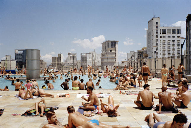 People crowding in and around a rooftop pool with skyscrapers visible in background