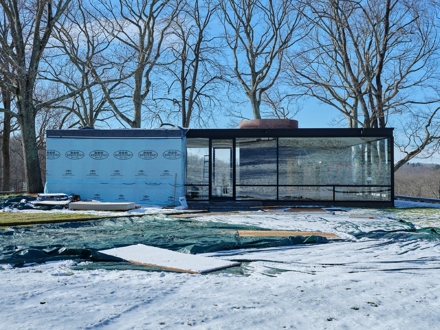 A winter photo of Philip Johnson's Glass House, half covered in tarps