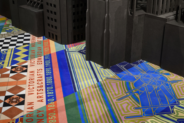 A closeup of a colorful carpet with dates and facts and the base of a black architectural model.