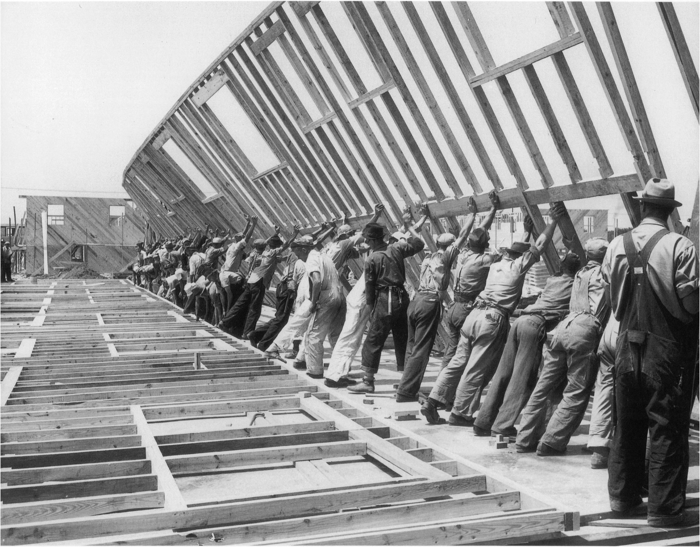 Black and white photo of men working together to raise a wood frame
