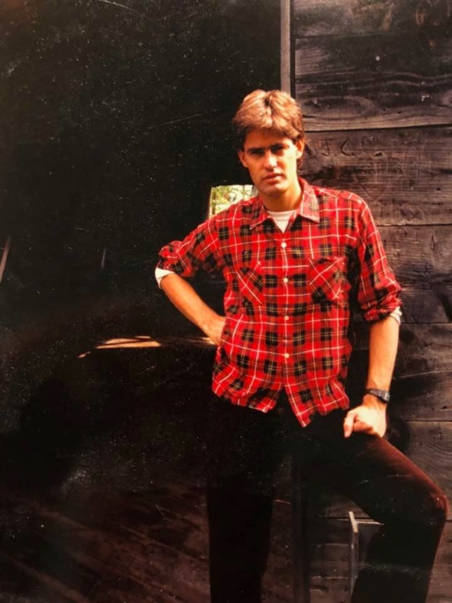A young man in flannel leaning against a wall