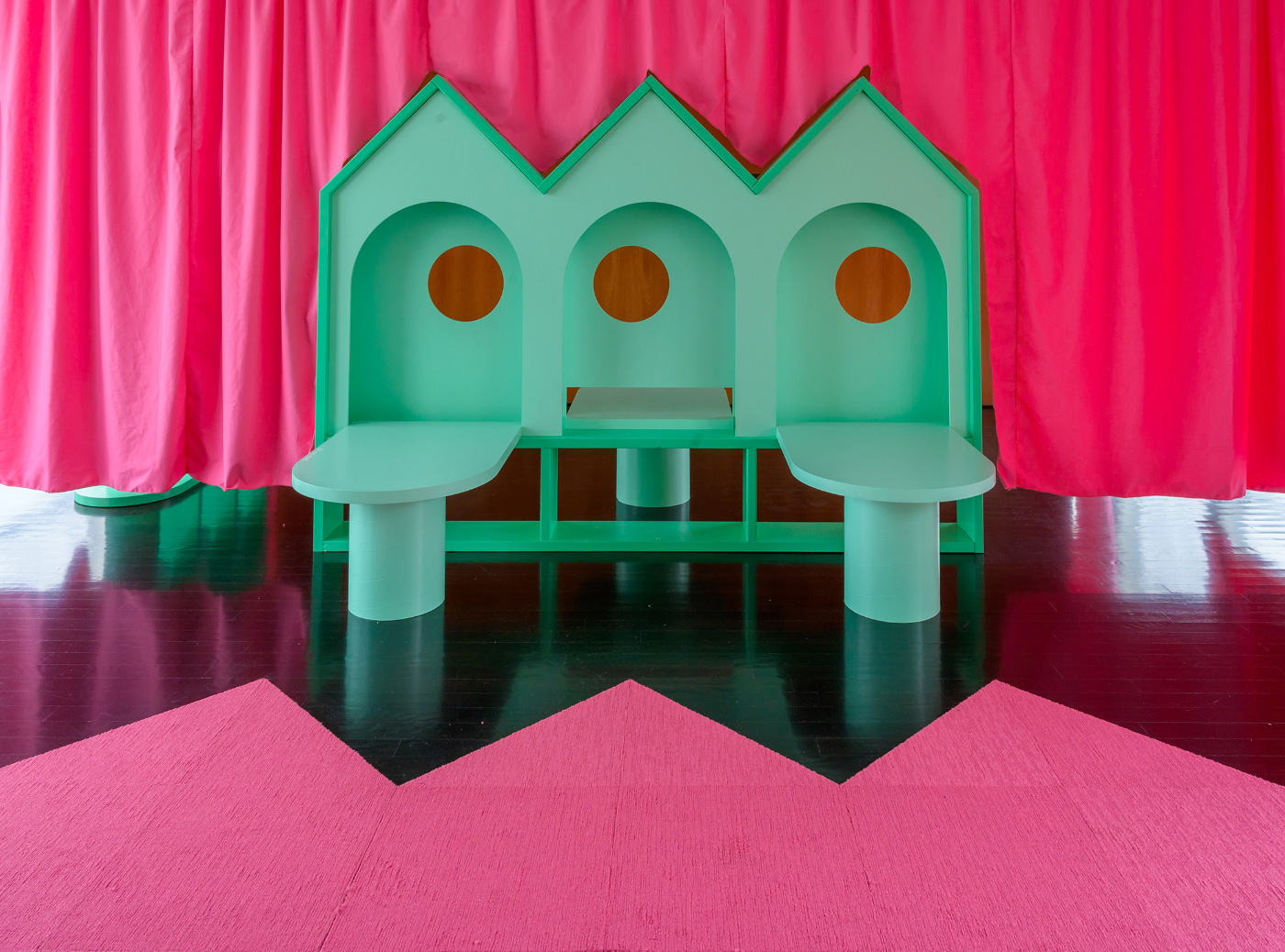 A green house-like piece of furniture in front of a pink curtain