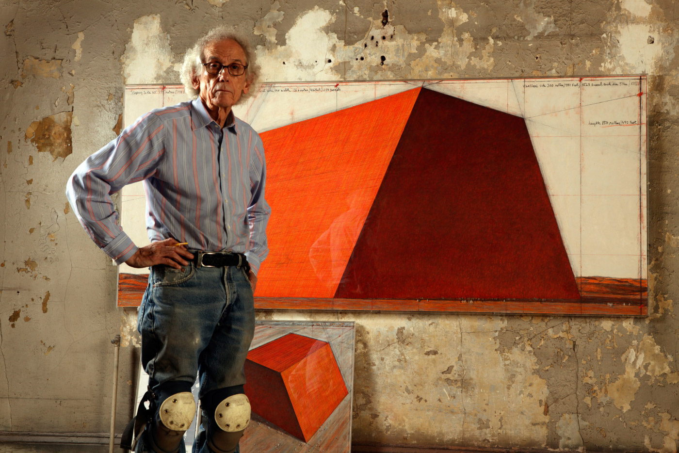 Artist Christo in front of a painting of an orange pyramid