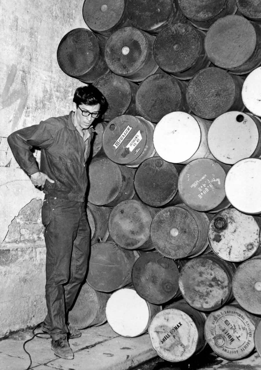 Black and white photo of Christo in front of oil barrels