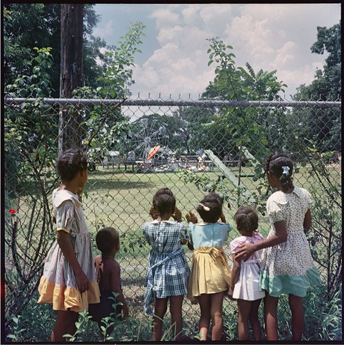 Photo of Black children looking through a chain link fence at an empty playground