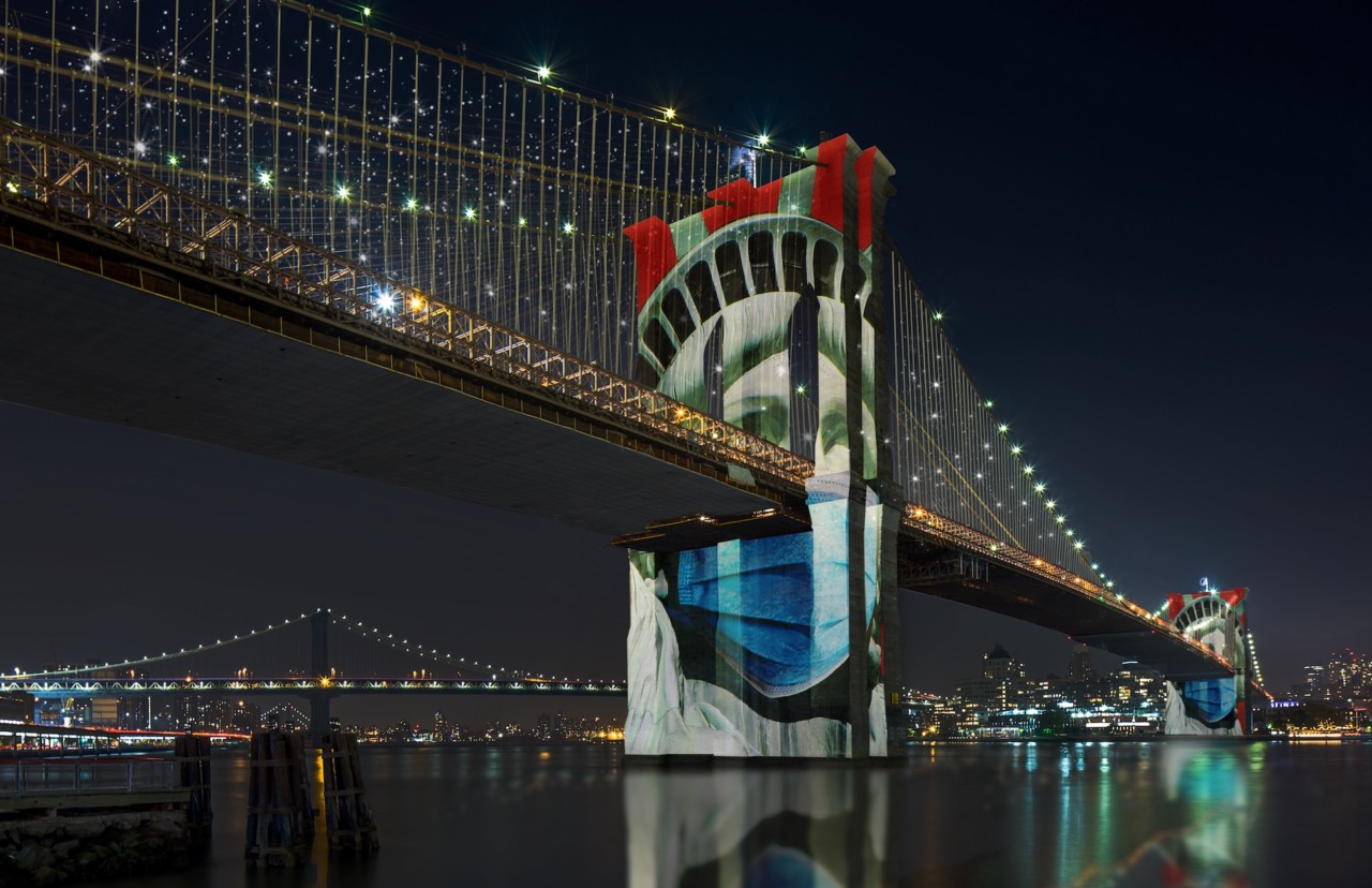 Brooklyn bridge lit up at night with the statue of liberty projected across