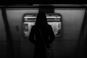 A greyscale photo of someone waiting for an MTA subway train
