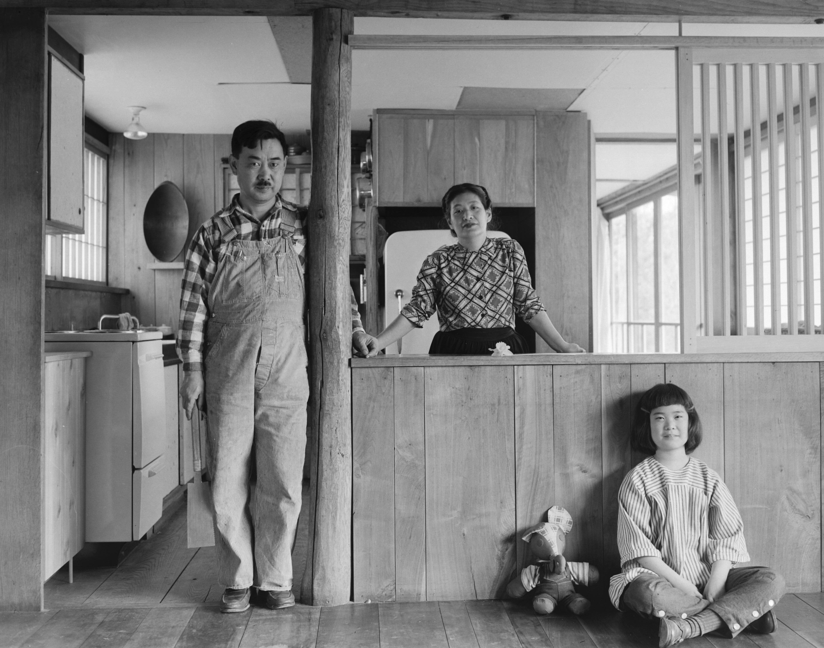 Black and white photo of a man, woman, and child in wood house