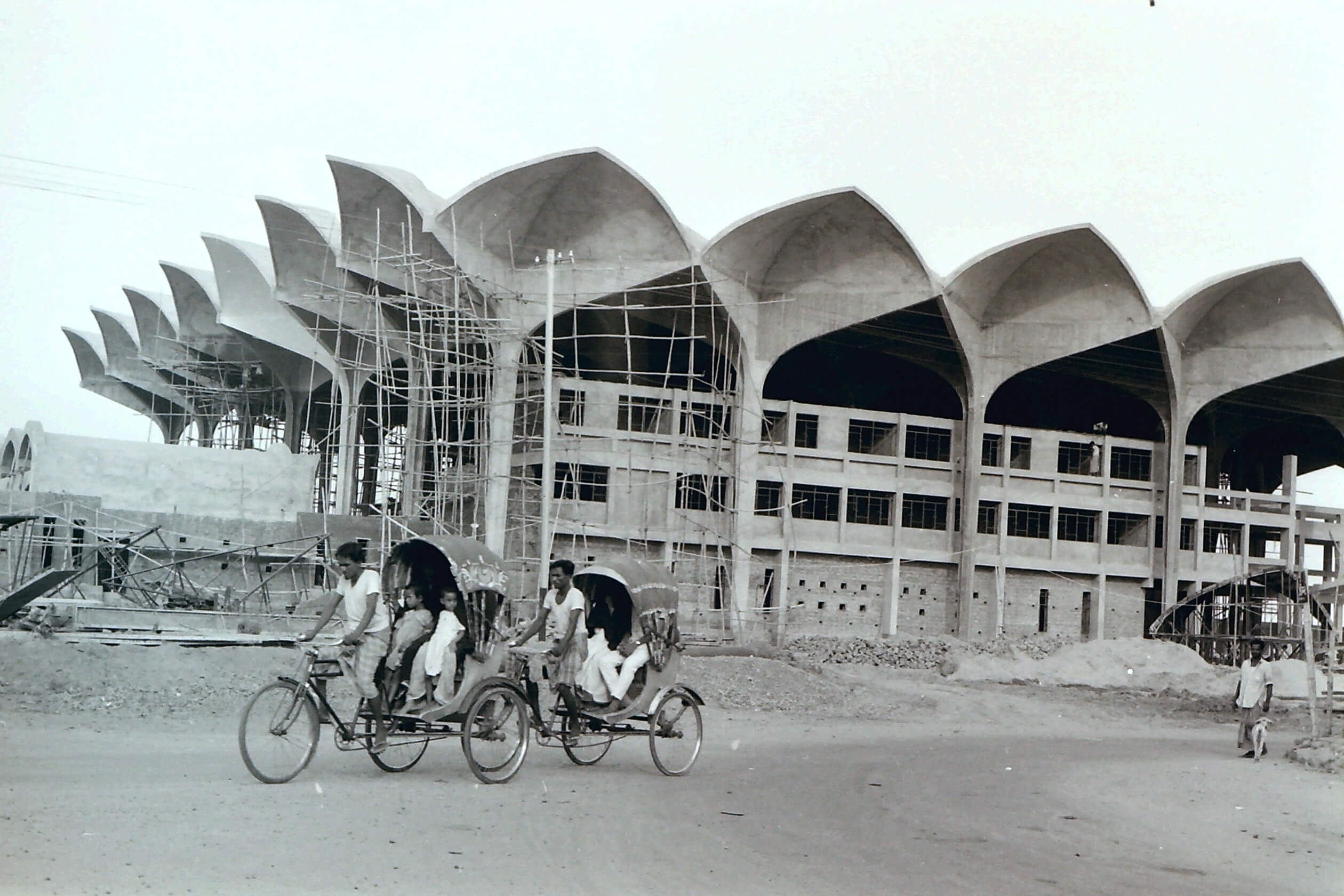 Black and white photo of people cycling past a train station under construction