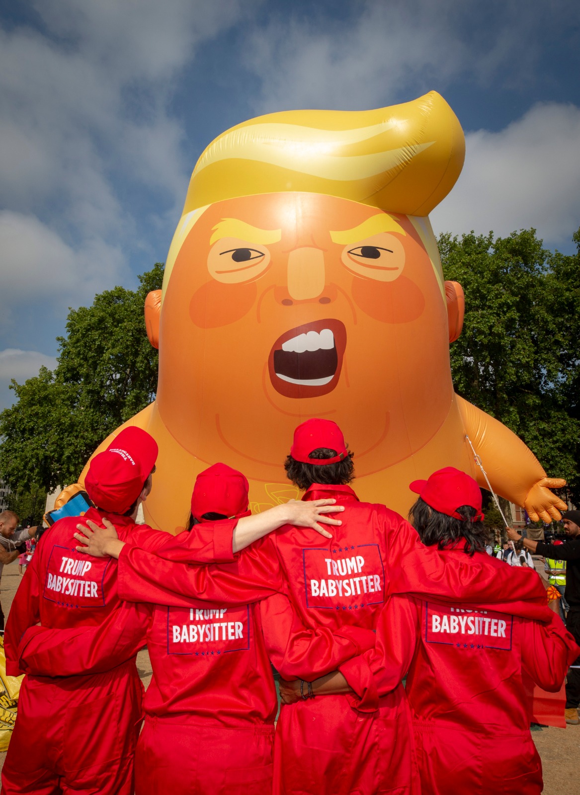 a crew in red in front of a trump baby balloon