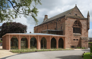 Exterior of Carlisle Cathedral, a red stone church with a low-slung arched atrium addition