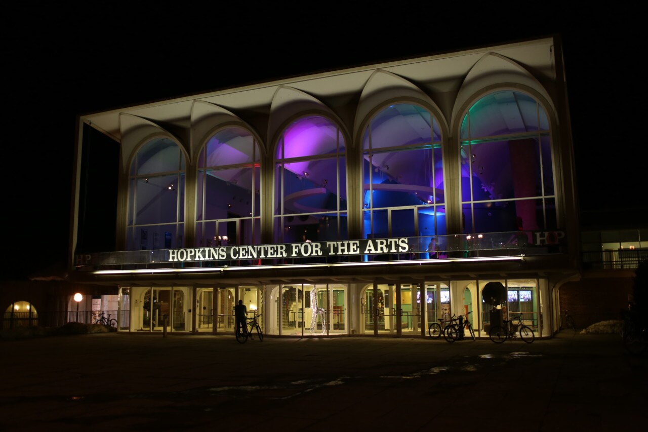 a college arts center pictured at night with "hopkins center for the arts" across its front