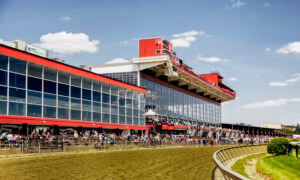 the Pimlico race track, fronted by a red glassy building with horses racing, part of the Preakness Stakes