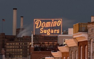 a lit neon sign atop a factory reading domino sugars