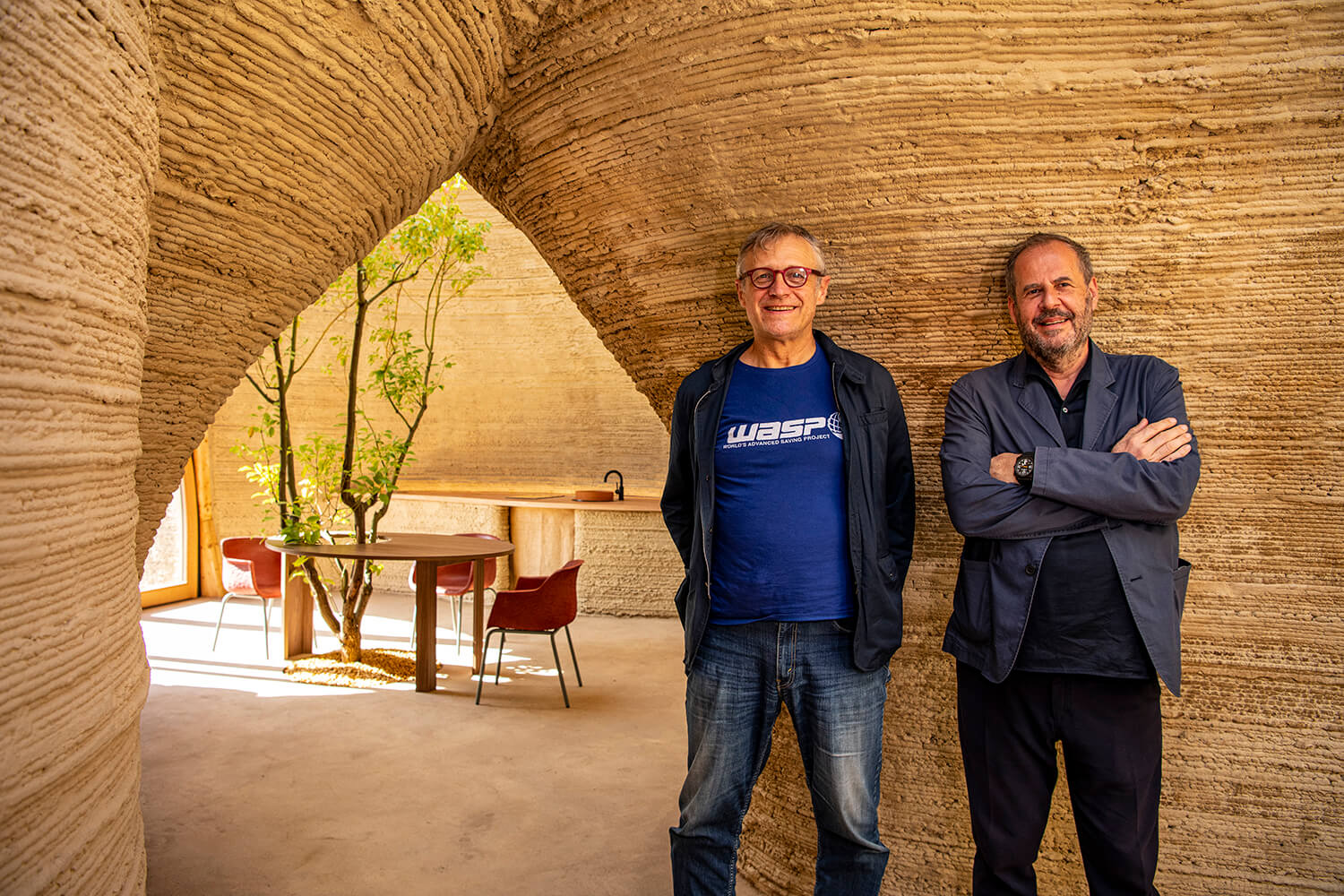 two men smile for a portrait inside an innovative clay home