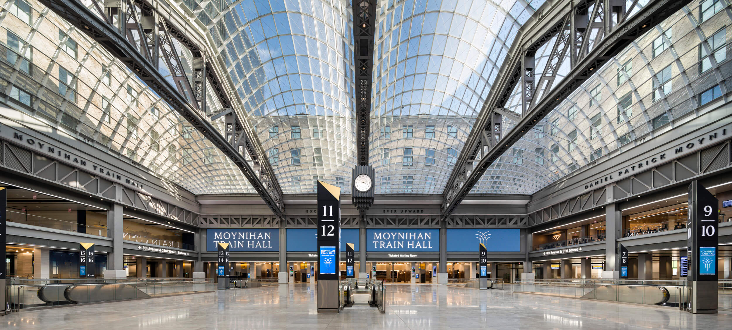 an interior photograph depicting a train concourse with a vaulted glass ceiling in moynihan train hall