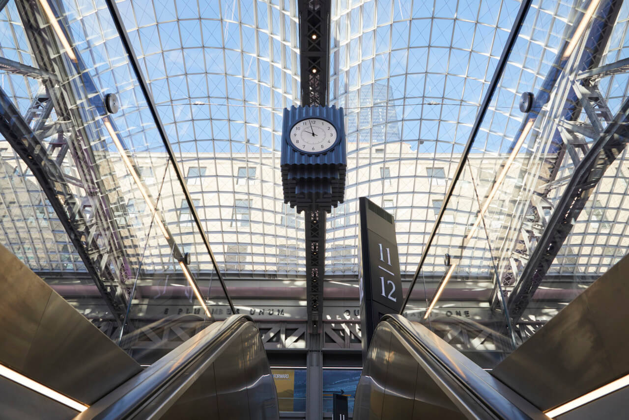 interior photograph of a contemporary train station with a suspended decorative clock at center in Moynihan train hall