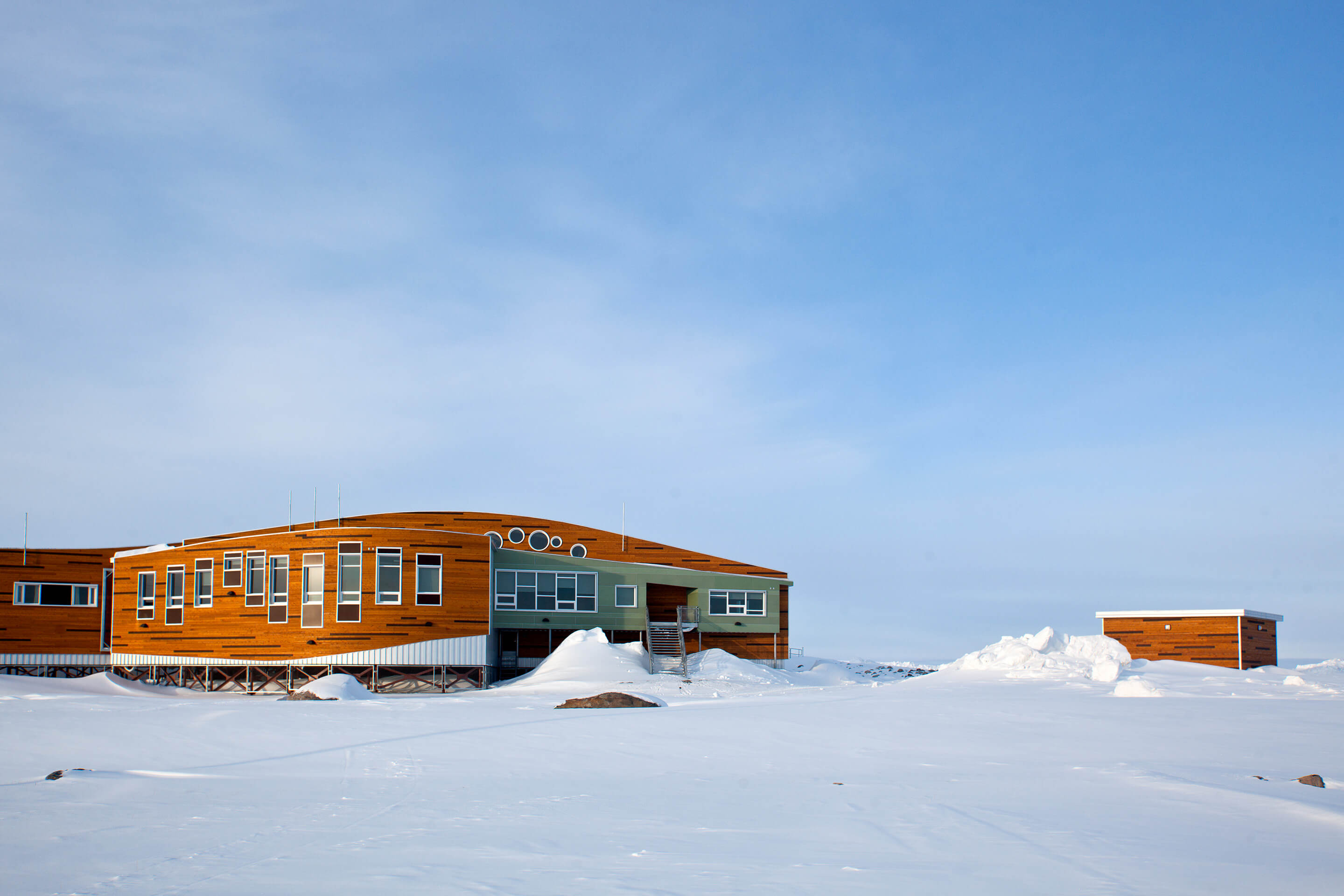 A timber building designed with a swooping massing sitting in the arctic snow