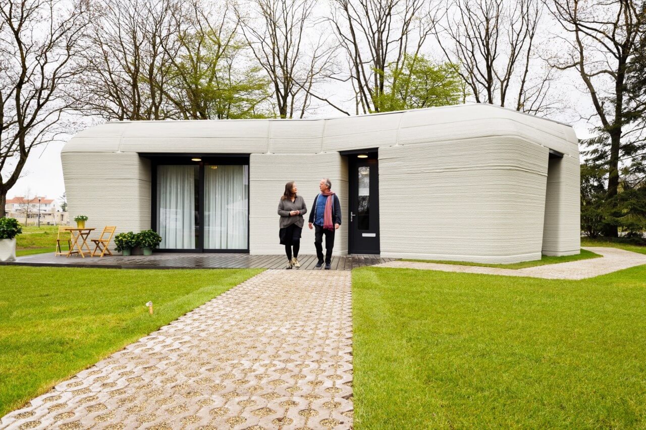 Two people walking in front of a boulder shaped 3d-printed house for today's daily digest