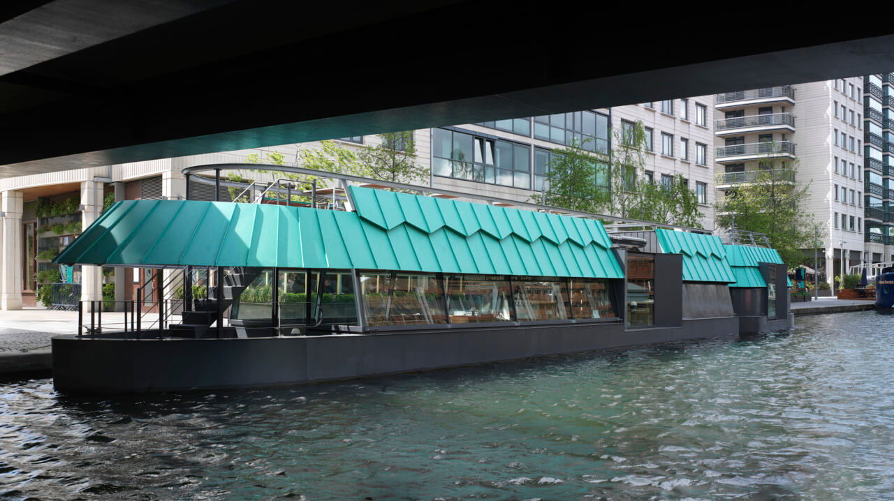 a barge-restaurant with a patinated roof as seen beneath a bridge
