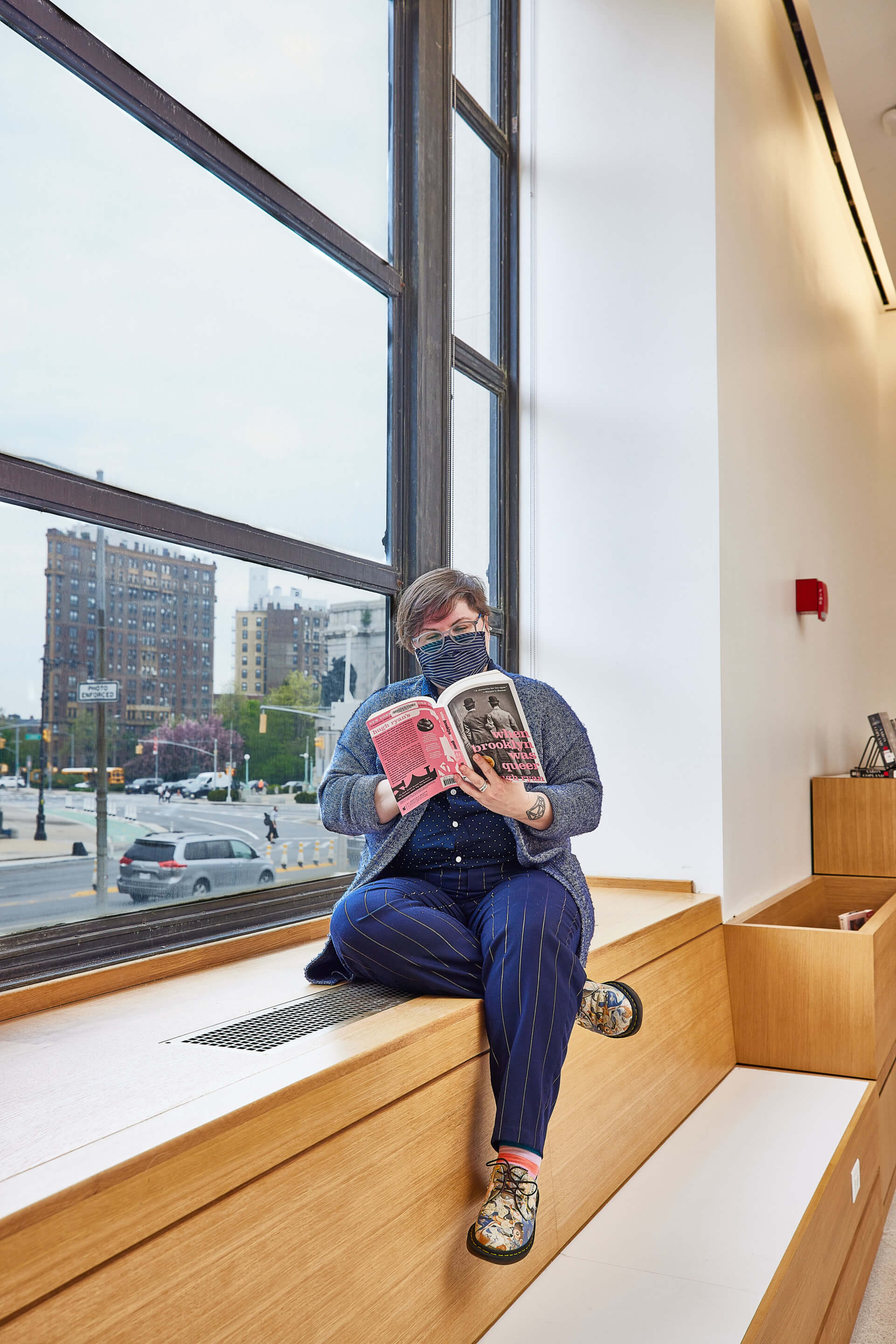 a woman sits on a windowsill reading a book in a public library