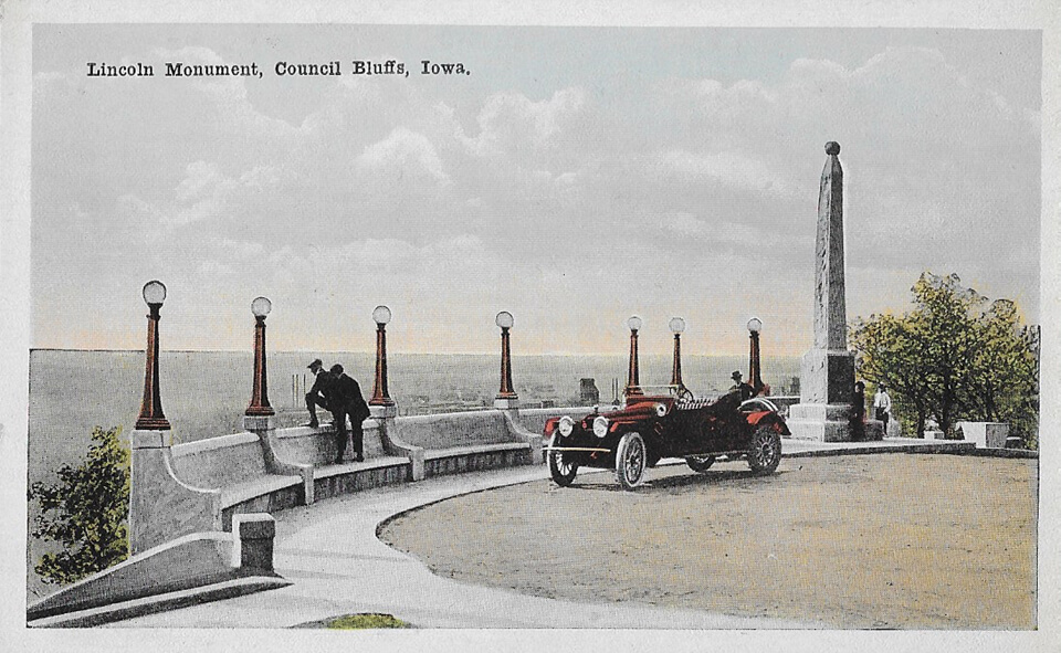 A postcard advertising council bluffs, showing a car at the edge of an overlook
