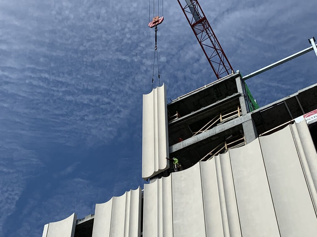 picture depicting a crane lifting a facade panel into place