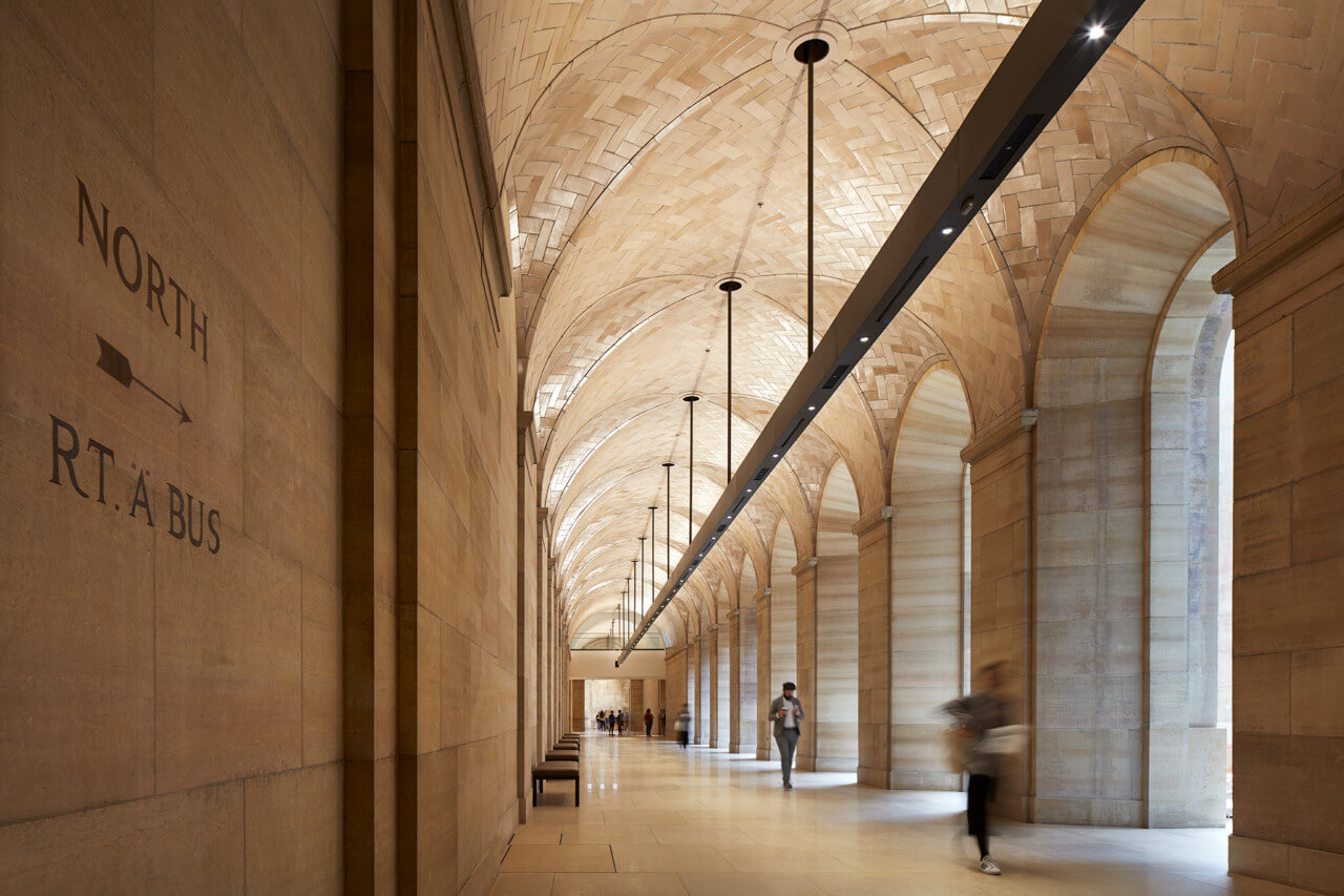 people walk beneath a tiled vaulted corridor