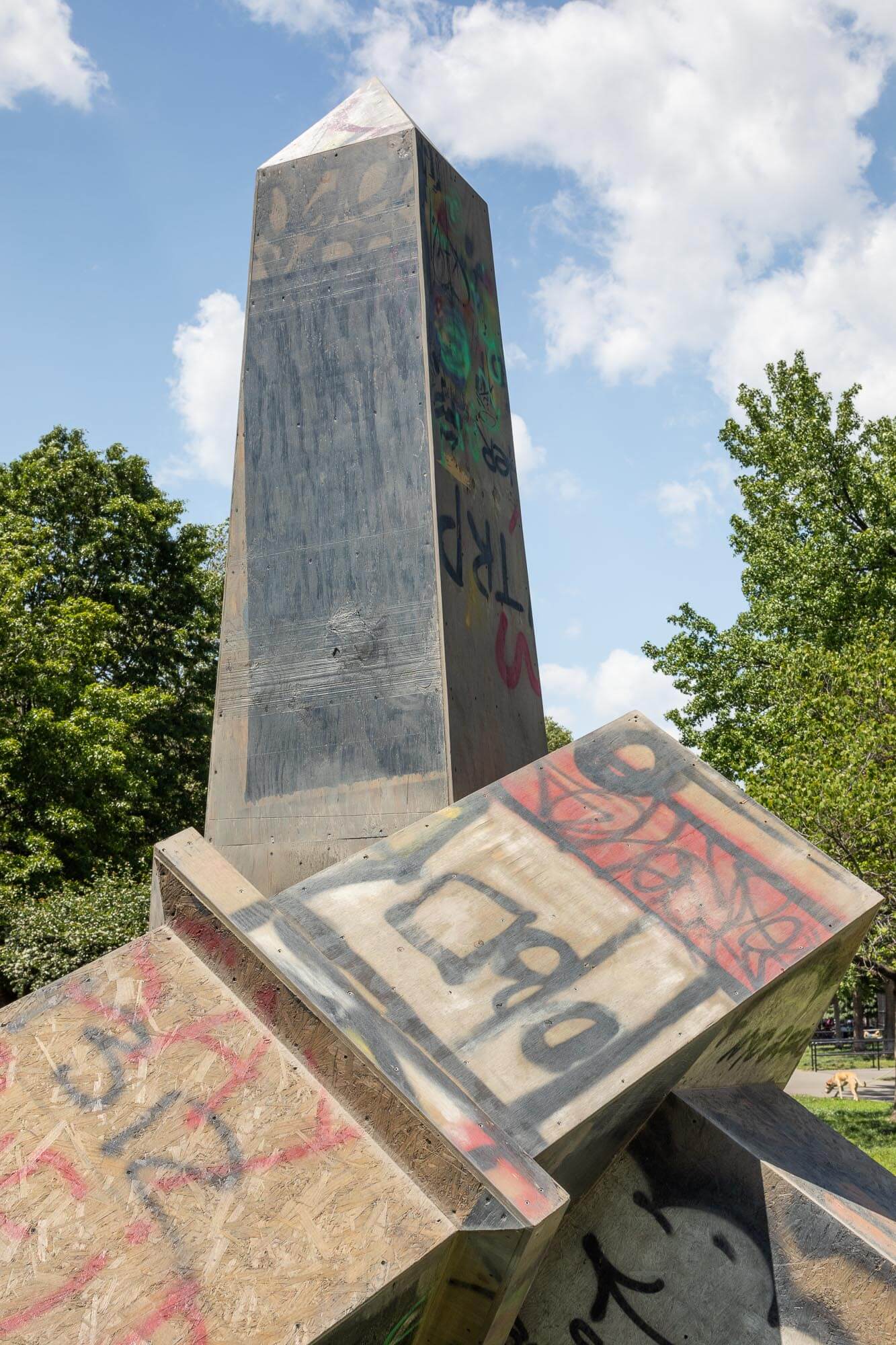 an abstract, graffiti-covered monument made from plywood in a park