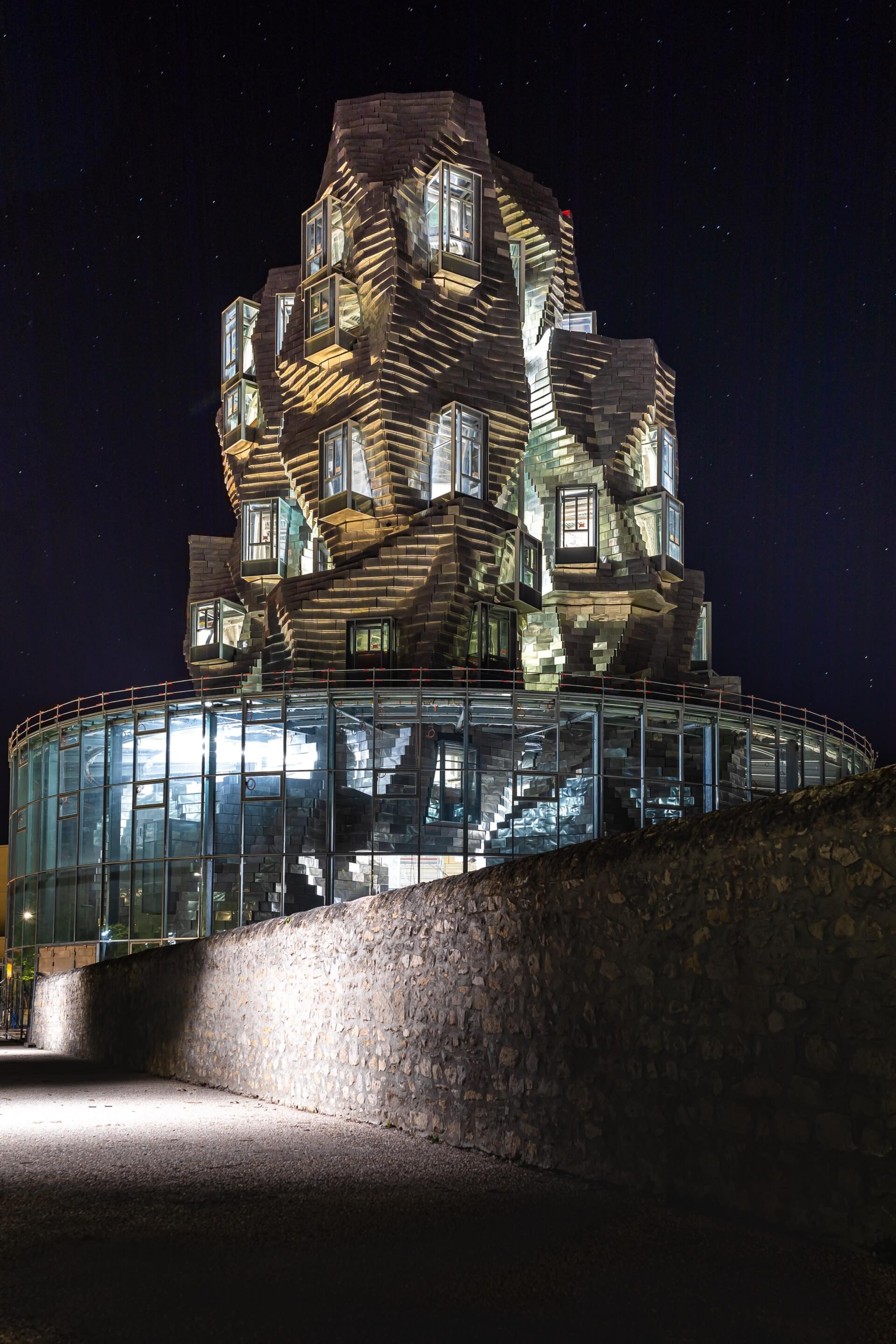 a twisting metal tower atop a circular structure, pictured at night at luma arles